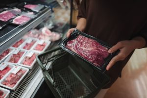 Woman holding a tray filled with fresh red meat while browsing the supermarket, carefully selecting ingredients for dinner